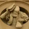 Skulptur aus Stein: Das Halbkörperporträt eines Geldboten der früheren Kassenhalle tritt aus einem ovalen Rahmen hervor. Der bärtige Mann hebt mit der rechten Hand seine Mütze zum Gruß. In der linken Hand hält einen Sack mit Münzen. Sein Umhang mit Puffär